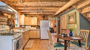 A cozy kitchen with wooden beams, a stove, cabinets, and a dining area with chairs and a table. - 'snowshoe Cabin' w/ Gas Grill: Fish & Hike! (Wasilla)
