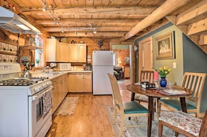 Una cocina acogedora con vigas de madera, una estufa, armarios y una zona de comedor con sillas y una mesa.