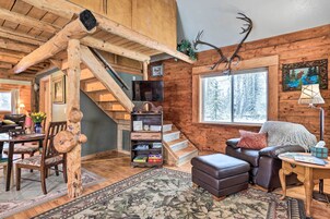 Interior rústico de una cabaña con escalera de madera, chimenea, televisor y un rincón de estar acogedor.
