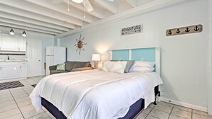 A bedroom with a large bed, a nightstand, a lamp, and a wall sign that reads "ADVENTURE". - Panama City Beach Studio w/ Pool & Beach Access (Panama City Beach)