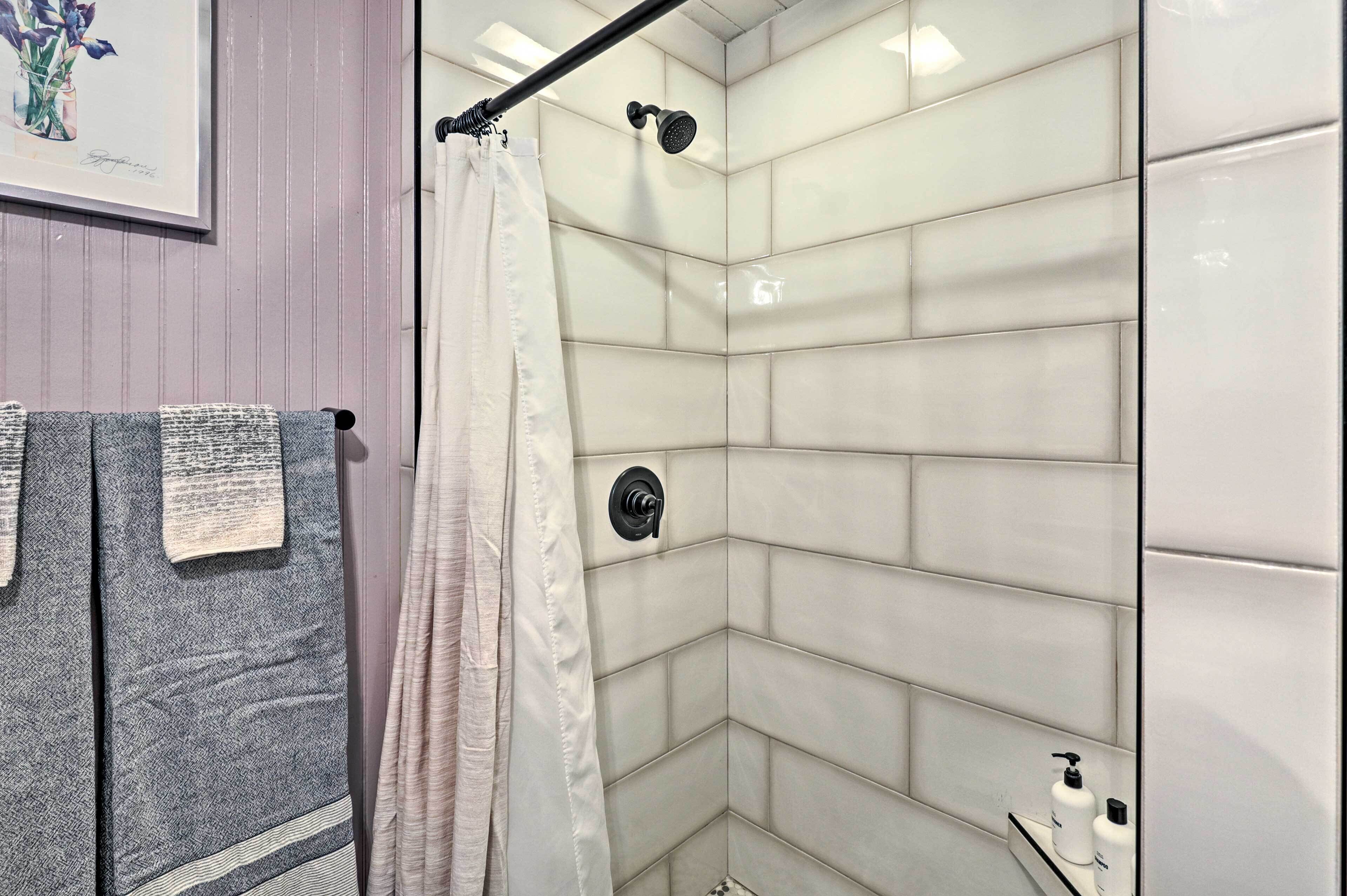A modern bathroom with a shower, white tiles, a towel rack with towels, and a framed picture on the wall.