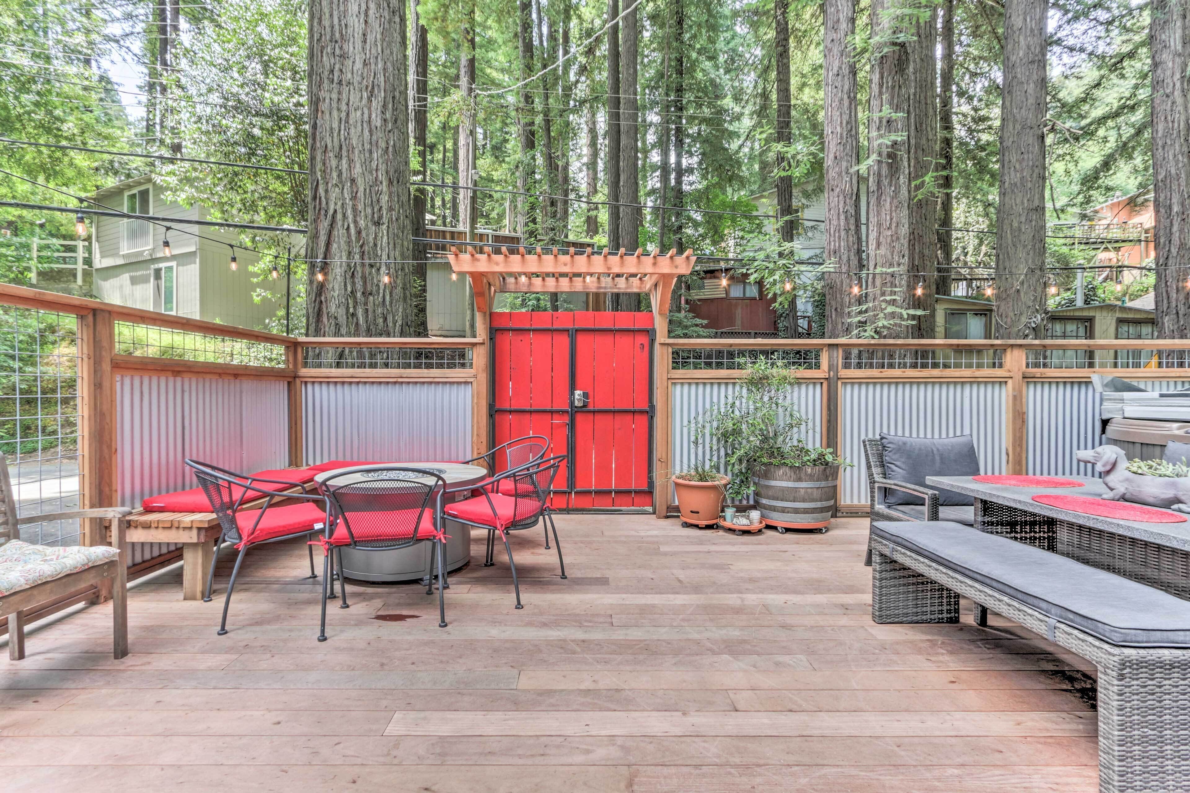 An outdoor patio with wicker furniture, a red gate, and tall trees in the background.