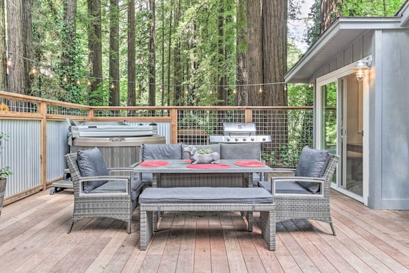 A deck with a table and chairs, surrounded by tall trees.
