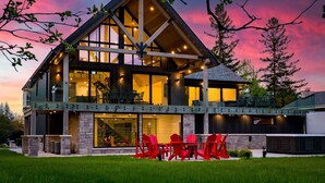 A modern house with a large deck, stone foundation, and large windows. - The Northern Escape HOT TUB & SAUNA! (blue mountain)