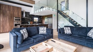 A modern living area with two dark blue sofas, a wooden coffee table, and a kitchen in the background. - The Northern Escape HOT TUB & SAUNA! (blue mountain)