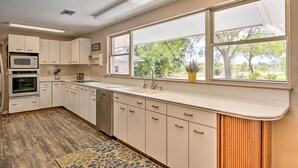 A kitchen with white cabinets, a microwave, an oven, a sink, and a window with a view of trees. - Riverfront Family Home: Yard, Orchard, Dock! (Los Fresnos)