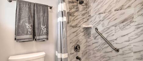 Ein Badezimmer mit Toilette, einer Duschkabine mit Haltegriff und Marmorfliesen.