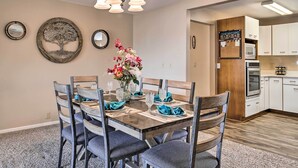A dining area with a wooden table set for six, surrounded by chairs. There is a chandelier above the table, and a wall-mounted mirror to the left. - Riverfront Family Home: Yard, Orchard, Dock! (Los Fresnos)