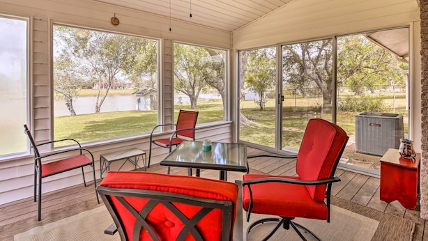 A covered patio with a table and chairs, large windows, and a view of a lake and trees. - Riverfront Family Home: Yard, Orchard, Dock! (Los Fresnos)