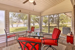 A covered patio with a table and chairs, large windows, and a view of a lake and trees. - Riverfront Family Home: Yard, Orchard, Dock! (Los Fresnos)