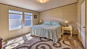 Une chambre à coucher avec un lit, deux tables de chevet avec des lampes, une fenêtre avec des stores, une porte et un tapis orné d’un motif circulaire.
