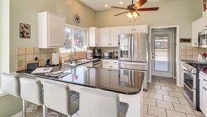 Una cocina amplia con una isla central, armarios blancos, electrodomésticos de acero inoxidable y un ventilador de techo.