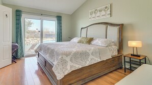 Un dormitorio con cama de madera, una mesita de noche con lámpara, una ventana con cortinas y una puerta que da a un balcón.