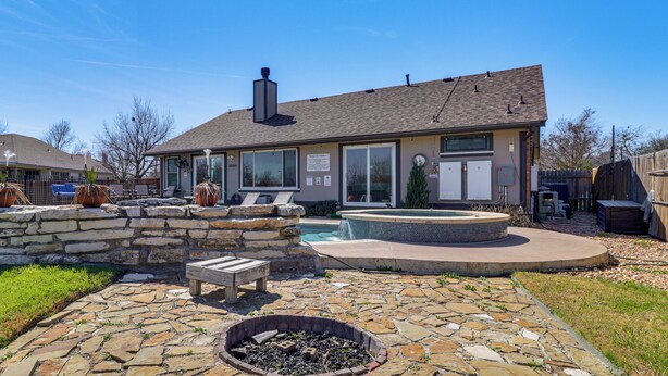 Una casa con patio de piedra, jacuzzi y piscina.