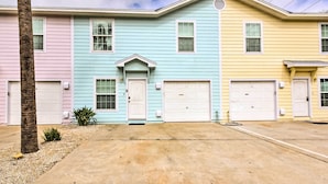 A row of three houses with pastel-colored exteriors and white garage doors. - Near Port Aransas Beach: Condo w/ Pool Access (Port Aransas)