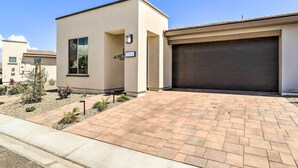 A modern residential building with a paved driveway, a garage, and a small garden area with shrubs and flowers. - Resort Pool & Hot Tub: 55+ Indio Desert Oasis (Indio)