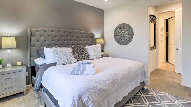 A bedroom with a large bed, a nightstand, a wall-mounted circular decoration, and a door leading to another room. - Resort Pool & Hot Tub: 55+ Indio Desert Oasis (Indio)