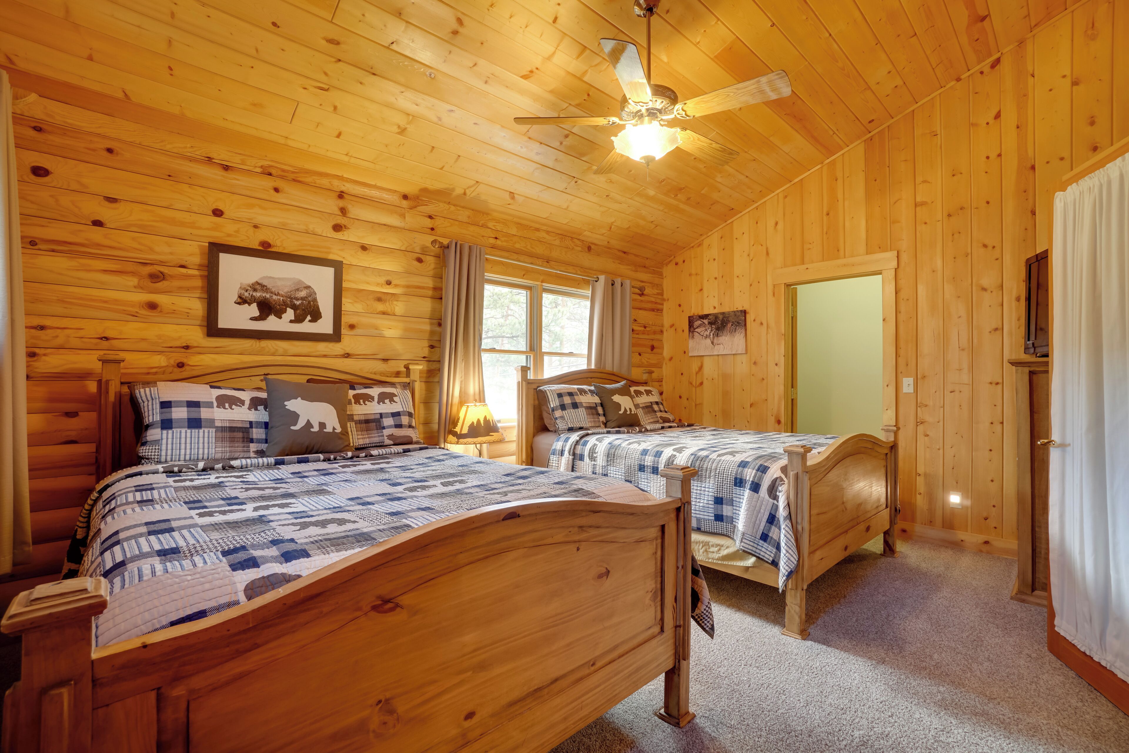 A wooden cabin bedroom with two beds, a ceiling fan, and a framed bear picture.