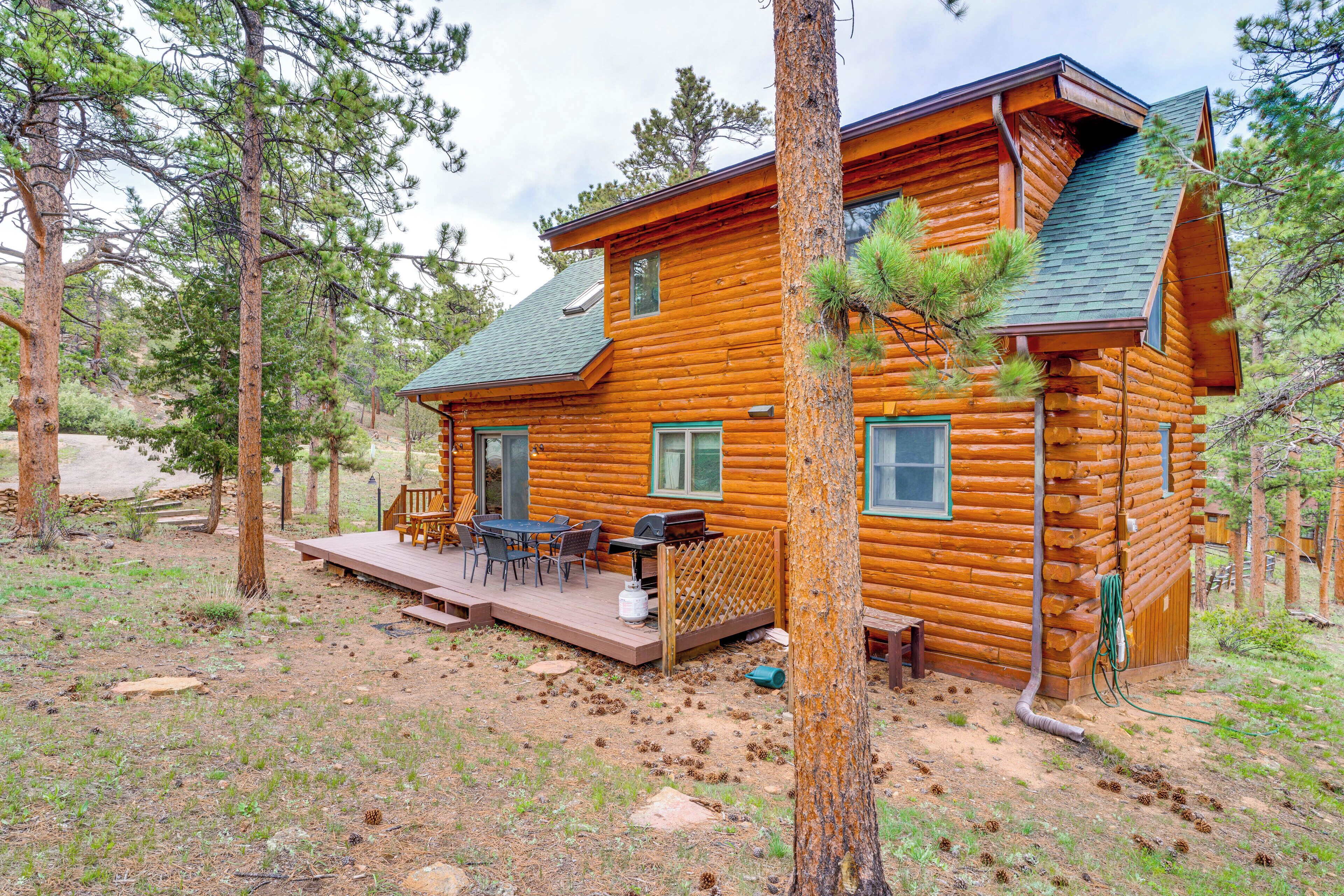 A log cabin with a deck, outdoor seating, and a view of the surrounding forest.