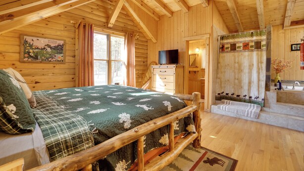 A wooden cabin bedroom with a bed, a television, and a bathroom with a shower curtain. - Picturesque Log Cabin in Estes Park: 9 Mi. to Rmnp (Estes Park)