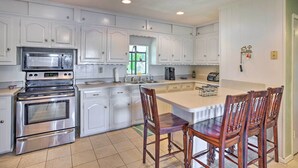 A kitchen with white cabinets, stainless steel appliances, a large island with chairs, and a window with a view. - Dock & Fire Pit: Waterfront Cedar Creek Lake Home (Kemp)