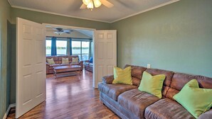 A living room with a brown leather couch, green cushions, a ceiling fan, and a view through an open door to a balcony with a sofa. - Dock & Fire Pit: Waterfront Cedar Creek Lake Home (Kemp)