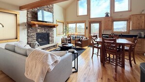 A spacious living area with a stone fireplace, a large sofa, and a dining area with wooden chairs and a table.