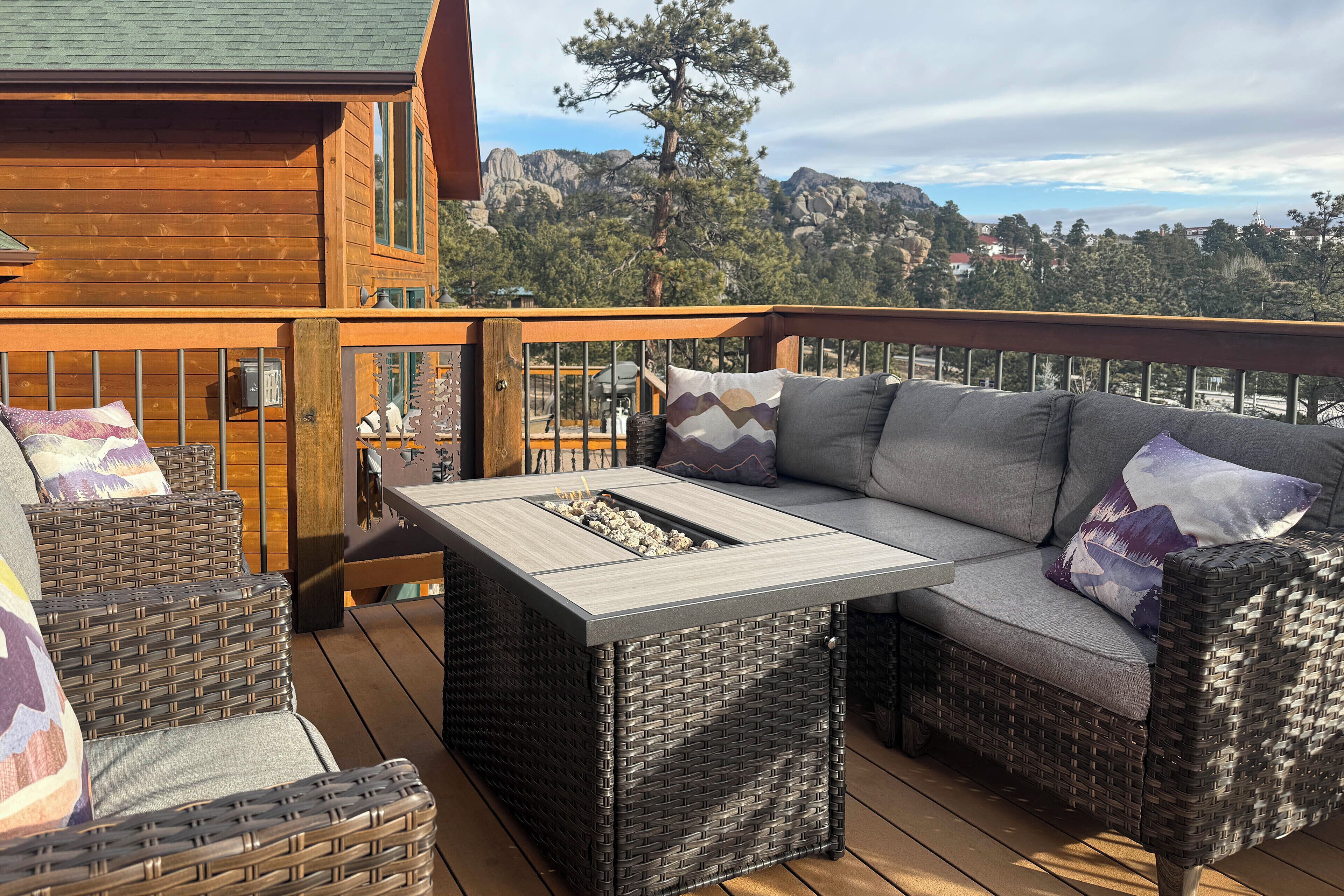 Une terrasse en bois avec des meubles en osier, un foyer intégré et une vue sur les montagnes.