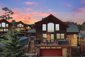 A large wooden cabin with multiple windows and a balcony, surrounded by trees and a mountain backdrop. - Updated & Spacious Lodge in Heart of Estes Park! (Estes Park)