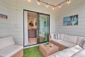 Ein modernes Wohnzimmer mit Glastür zum Balkon, einer Sofagarnitur, einem Couchtisch mit Früchten und einem Gemälde mit Strandmotiv.