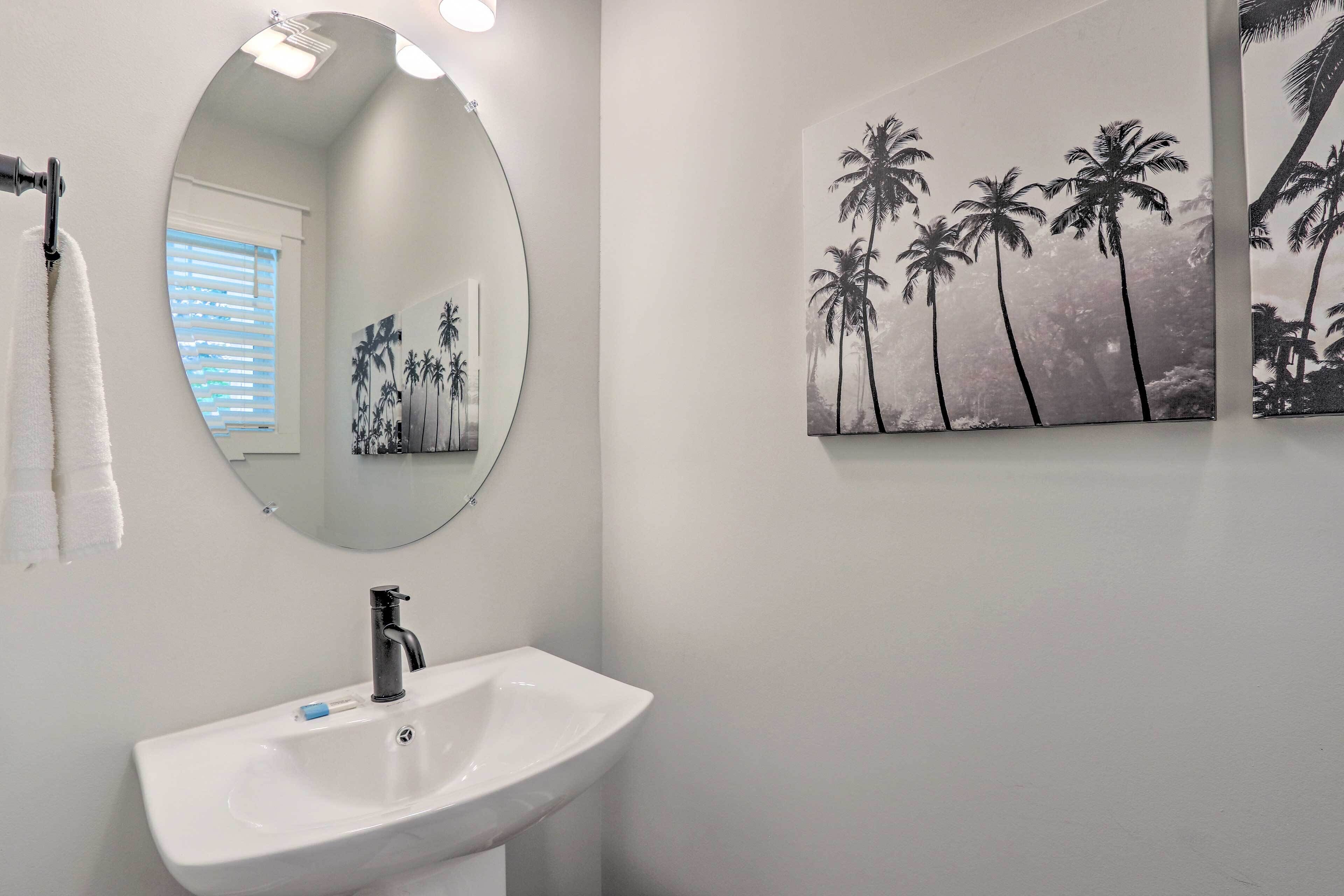 A bathroom with a white sink, a round mirror, and a painting of palm trees.