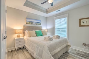 A bedroom with a large bed, a nightstand, a lamp, a ceiling fan, and a window with blinds.