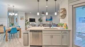 A modern kitchen with a dishwasher, a dining area with blue chairs, and a large window with blinds. - 4 Mi to Beach: Family-friendly Hilton Head Retreat (Hilton Head Island)