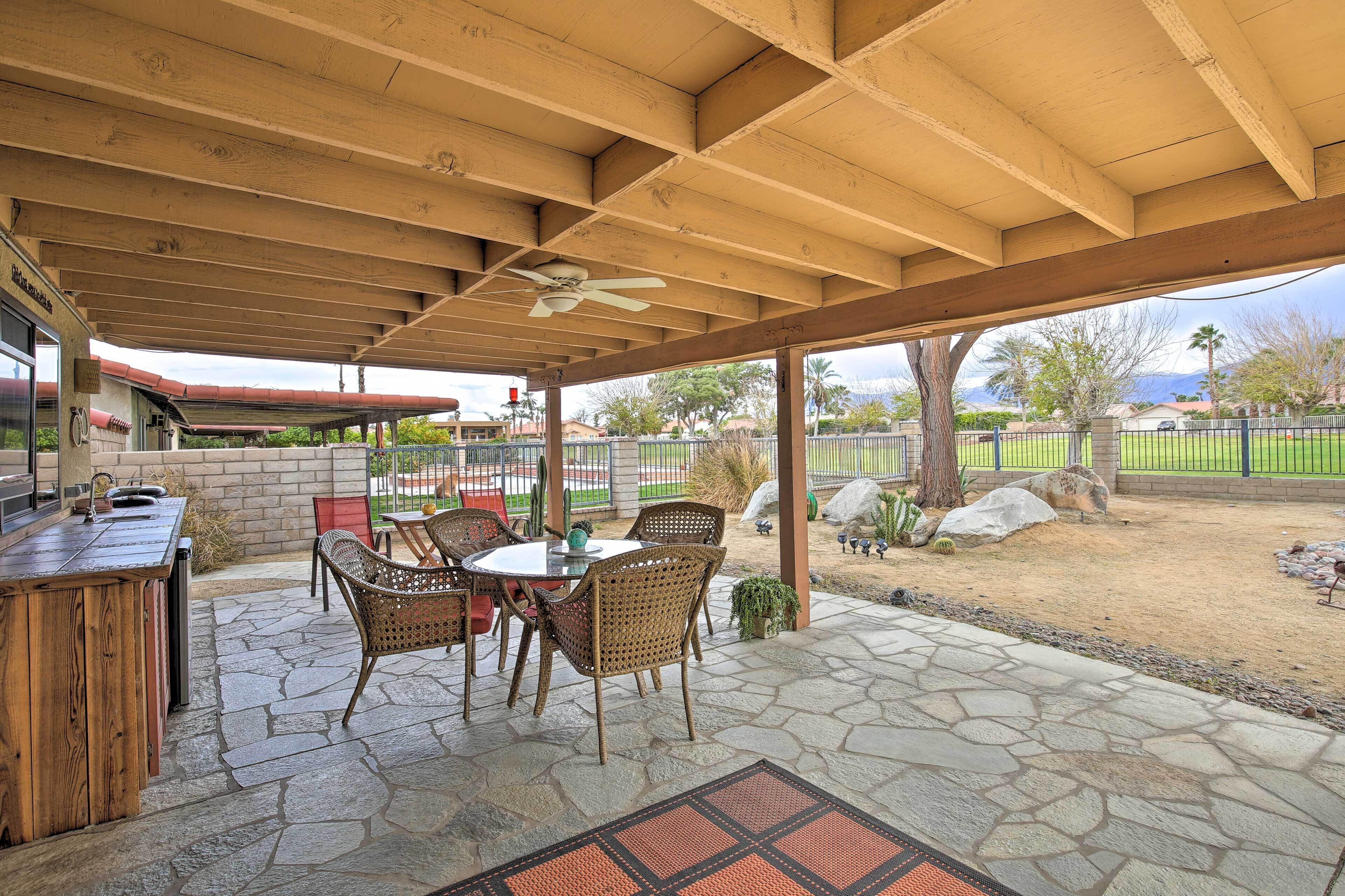 An outdoor patio with a wooden ceiling, stone flooring, and a table with chairs.