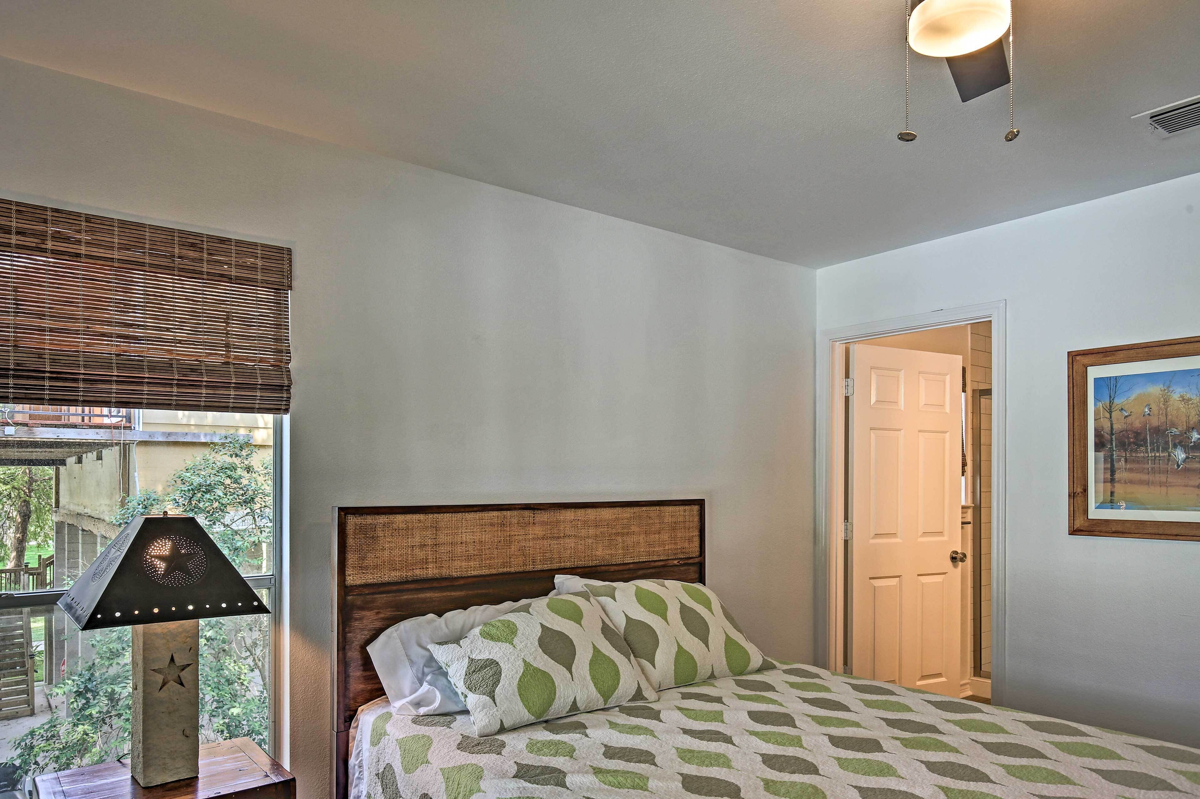 Un dormitorio con cama, mesita de noche, lámpara, ventana con persianas y puerta.