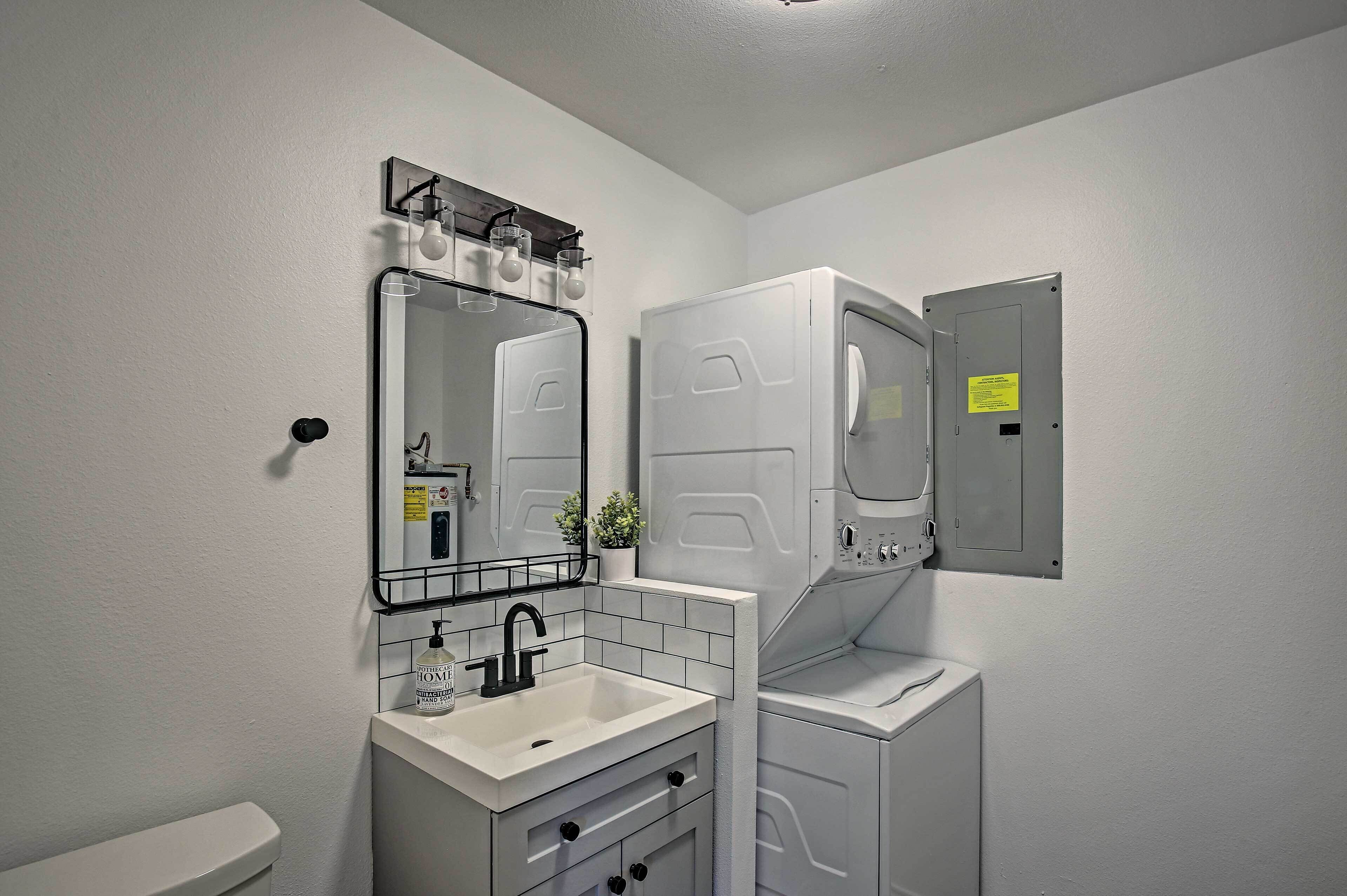 A modern bathroom with a white sink, mirror, and toilet. There is a small plant on the sink counter and a light fixture above the mirror.
