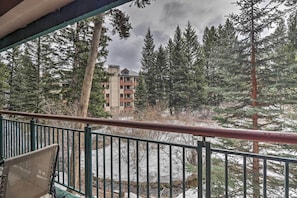 A balcony with a view of a building surrounded by tall evergreen trees.