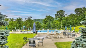 A poolside area with lounge chairs and umbrellas, surrounded by greenery and trees. - Pocono Retreat, 1 Mi to State Park & Ski Access! (Tannersville)