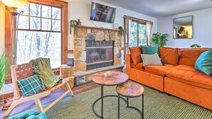 A cozy living room with a stone fireplace, a comfortable orange sofa, and a wooden bench. - Pocono Retreat, 1 Mi to State Park & Ski Access! (Tannersville)