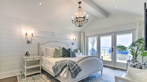 A bedroom with a large bed, a chandelier, a nightstand, and a view of the outdoors.