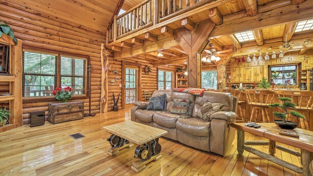 L’intérieur d’une cabane en rondins, avec un plancher en bois, un canapé en cuir, un coin repas et une cuisine dotée de meubles en bois.