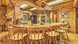 L’intérieur d’une cabane en rondins, avec une table à manger en bois, des chaises, un coin cuisine et une cheminée.