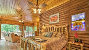 Une chambre située dans un chalet en rondins, avec un grand lit, une tête de lit en bois et une vue sur l’extérieur.