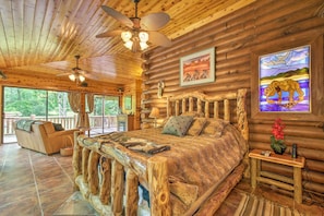 A log cabin bedroom with a large bed, wooden headboard, and a view of the outdoors. - Log Cabin Sanctuary in Inverness w/ Furnished Deck (Inverness)