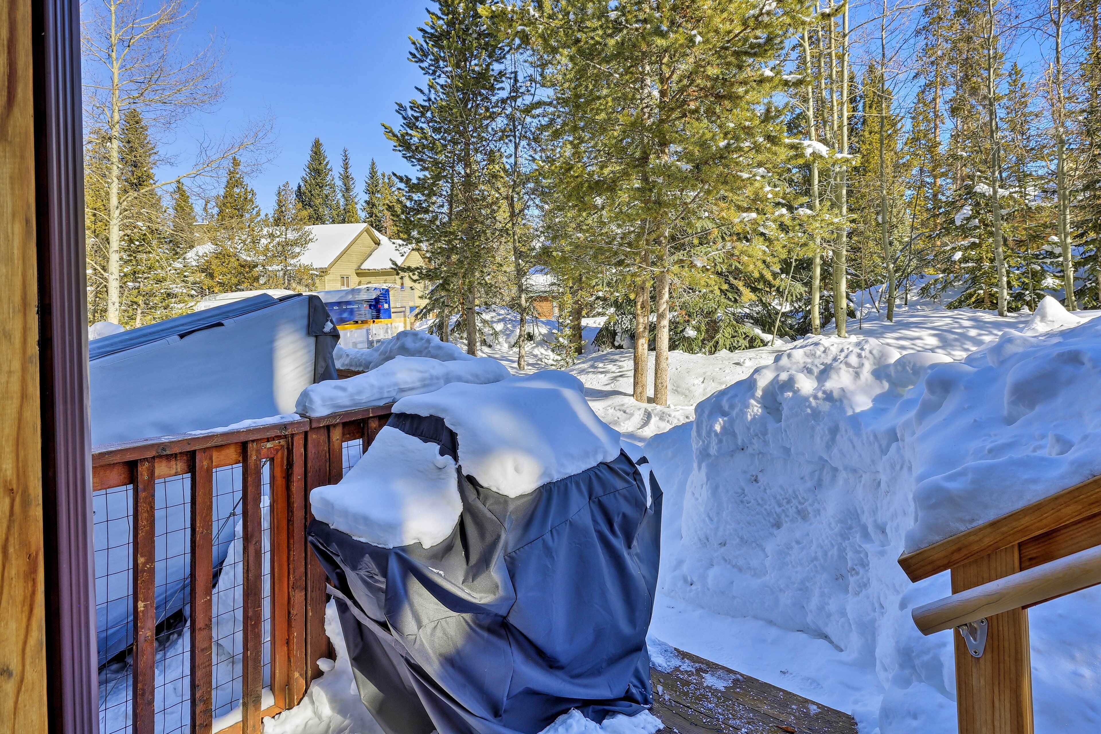 Un espacio exterior nevado con una terraza de madera, un objeto cubierto y una casa al fondo.