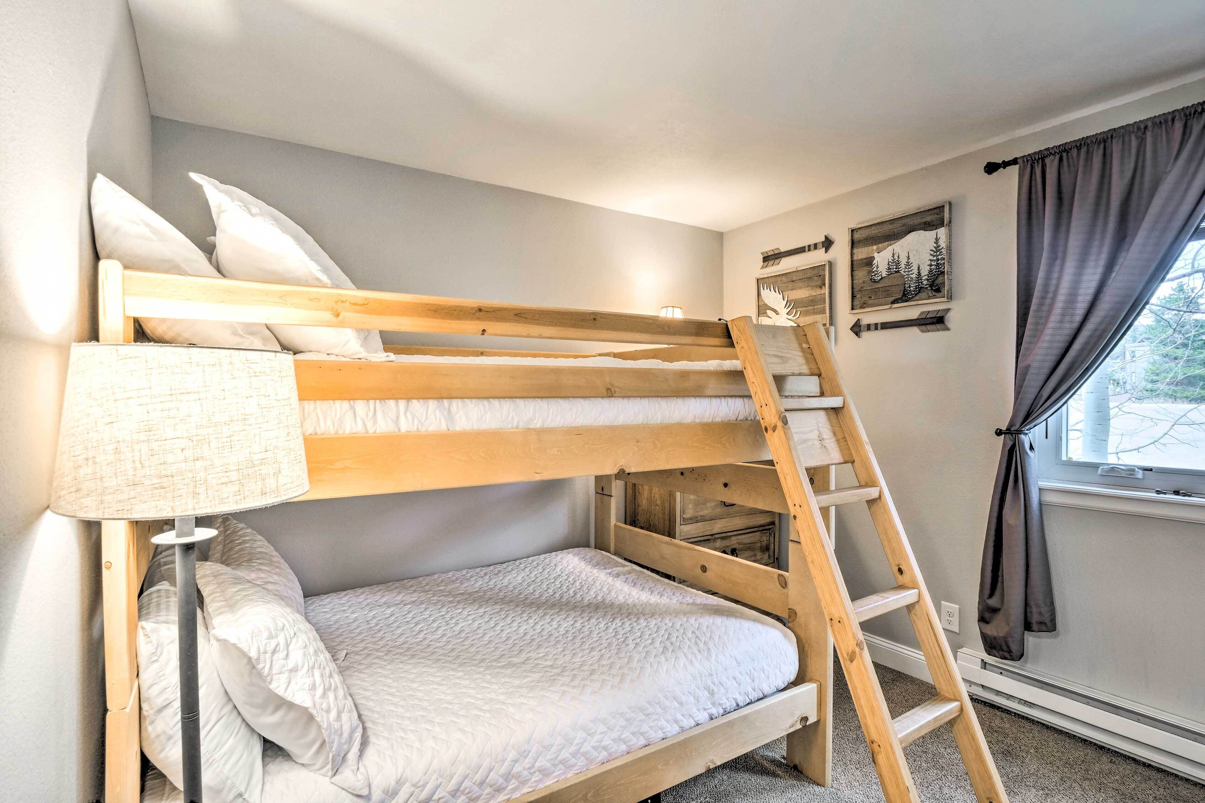 Una cama litera con escalera, una lámpara de noche y una ventana con cortinas.