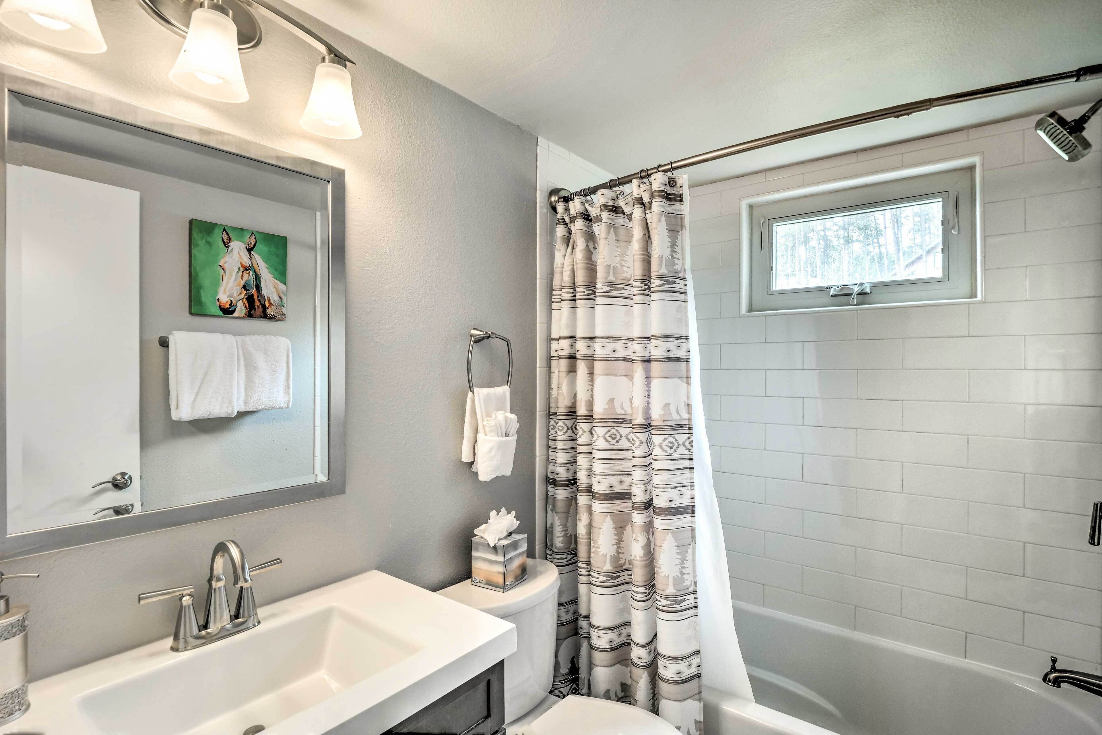 A bathroom with a white sink, a mirror, a towel rack, a toilet, and a shower with a patterned curtain.