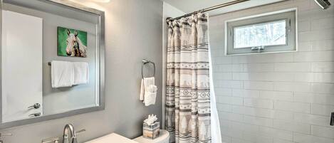 A bathroom with a white sink, a mirror, a towel rack, a toilet, and a shower with a patterned curtain.
