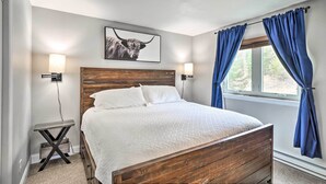 Een slaapkamer met een houten bed, witte beddengoed, een hoofdeinde, twee wandlampen, een lijstwerk met een afbeelding van een stier en blauwe gordijnen.