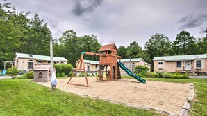 Ein Spielplatz mit Schaukel und Rutsche, umgeben von grünem Gras und Bäumen.